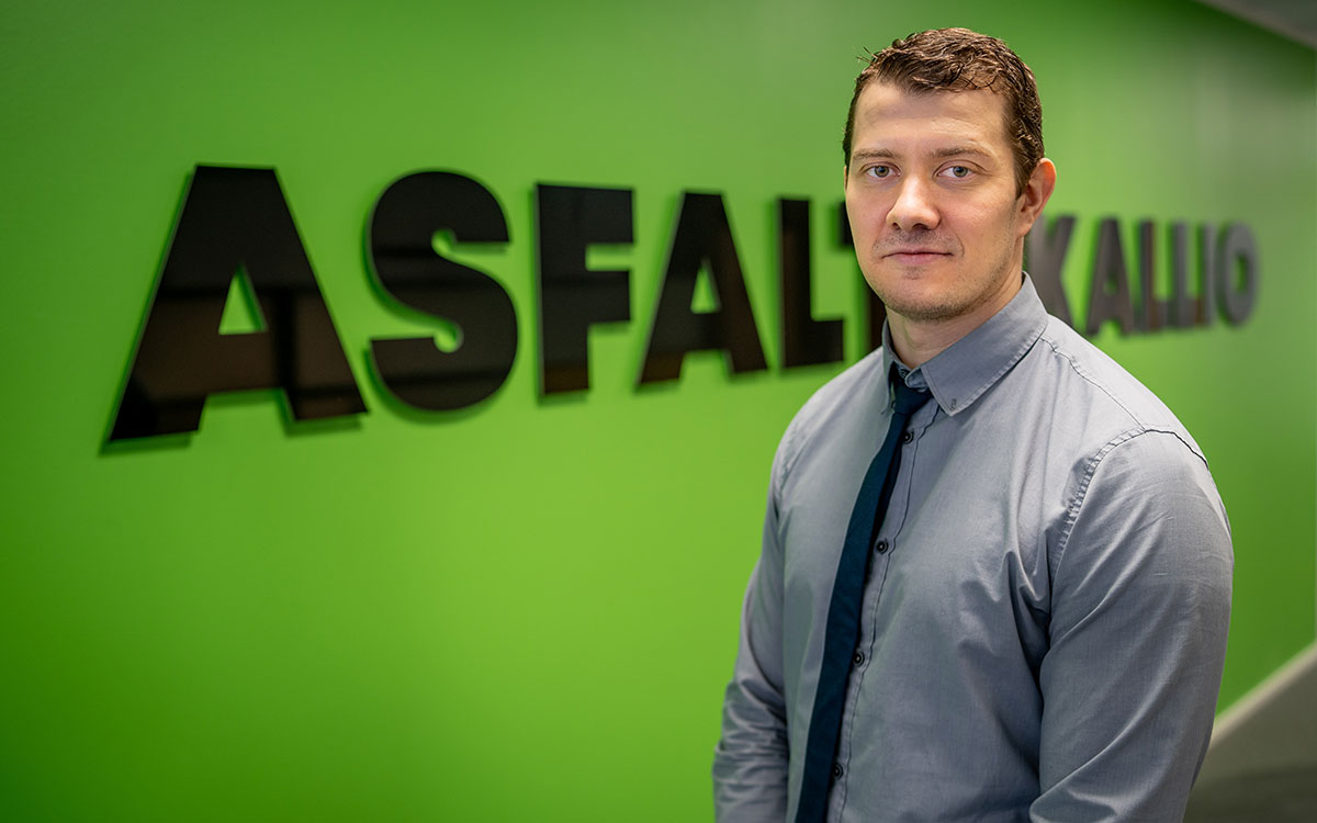 Linkityn asiakkaan Asfalttikallio Oy:n talousjohtaja Tuomas seisoo vihreän seinän edessä, jossa lukee asfalttikallio